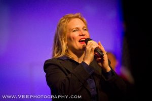 A woman singing into a microphone at an event.