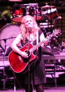 A woman playing an acoustic guitar on stage.