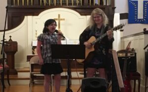 Four people singing outdoors in winter with songbooks.