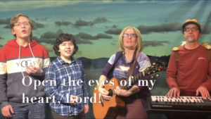 Four people singing outdoors in winter with songbooks.